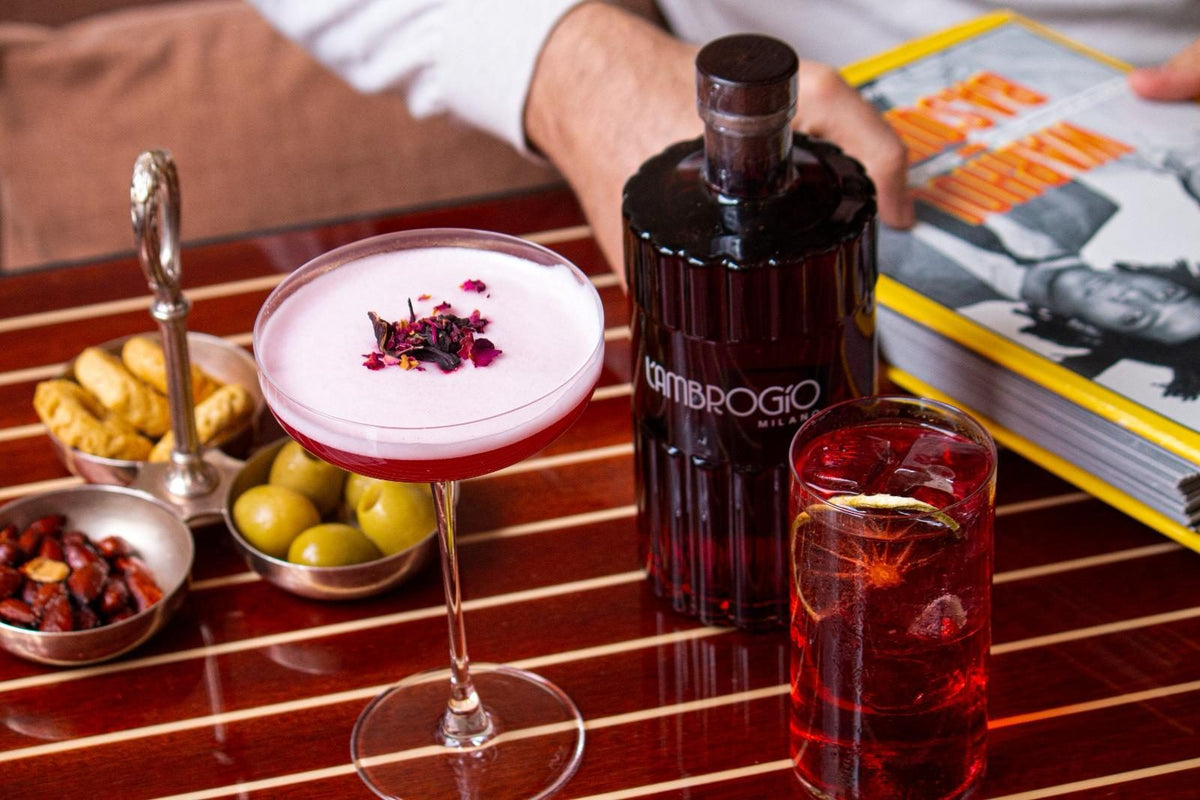 Bottiglia di L'Ambrogio Milano sul bancone con cocktail e stuzzichini per l'aperitivo